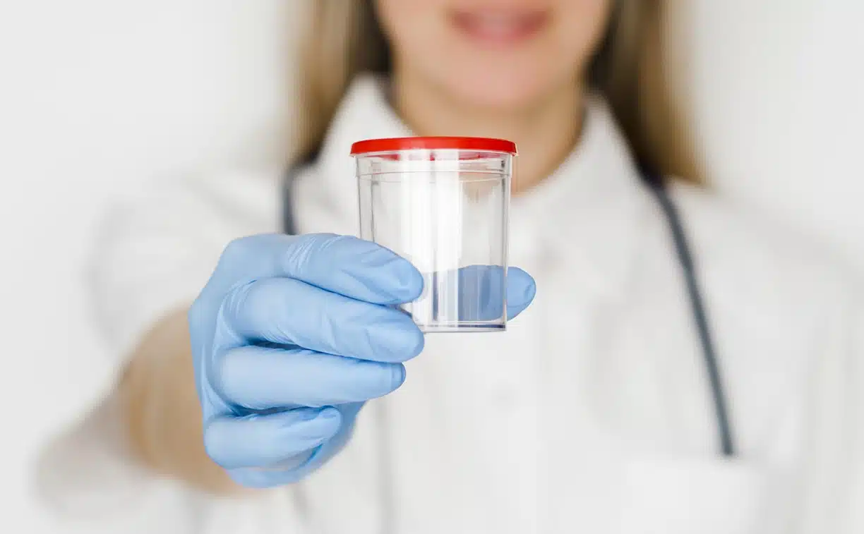 Woman in white a coat and wearing blue gloves holding a collection jar